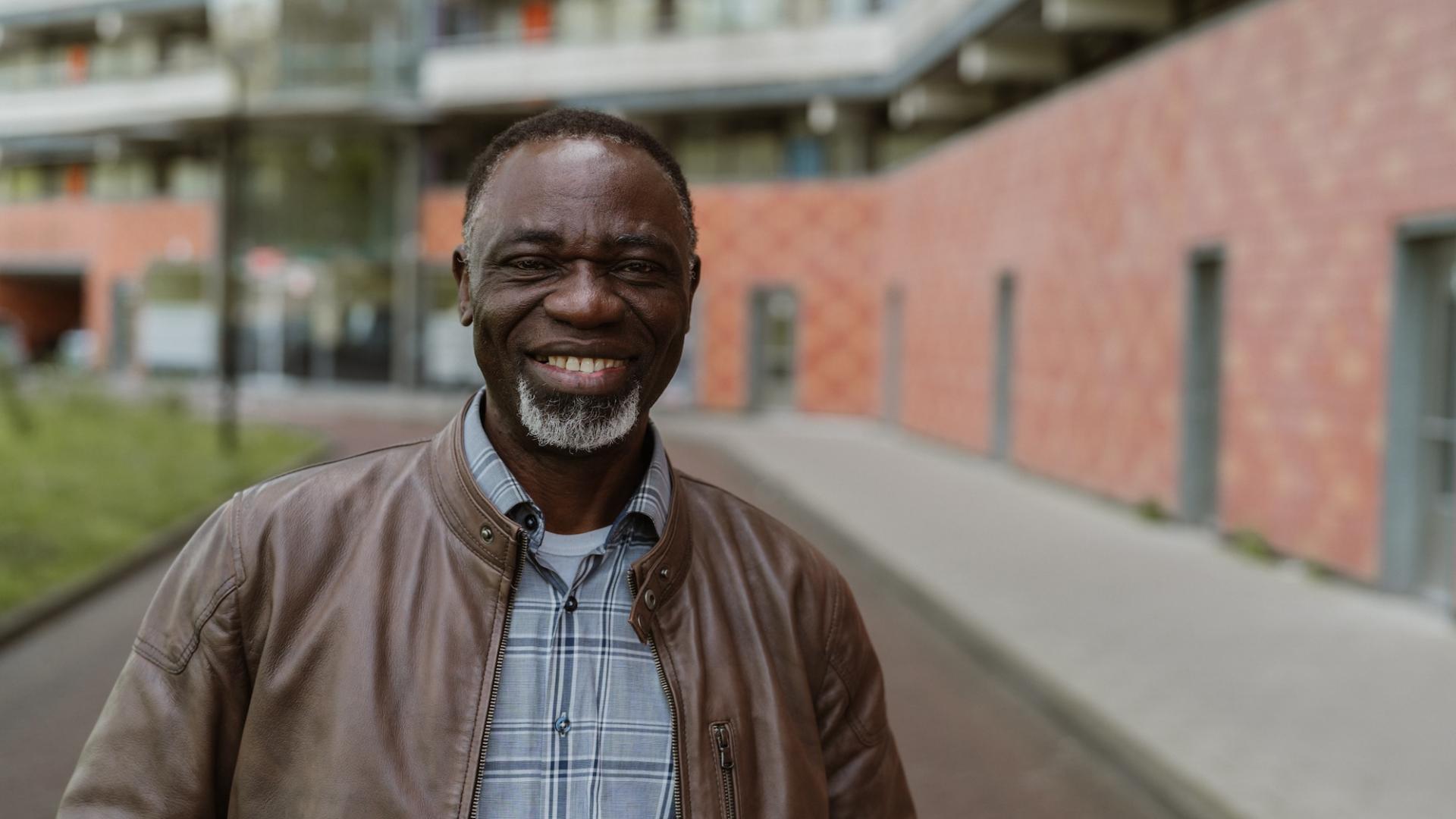 Moses staat voor een flatgebouw in Amsterdam Zuidoost. Hij kijkt lachend in de camera.