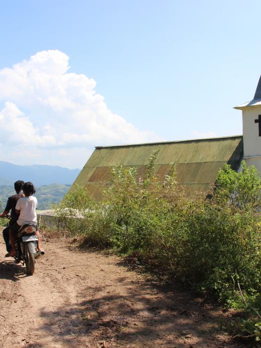 Twee personen op scooter langs een kerk in Indonesie